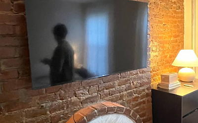 A 65" tv mounted over an old and weather brick fireplace.