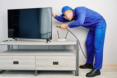 Technician organizing TV cables behind a wall-mounted TV — professional cable management service